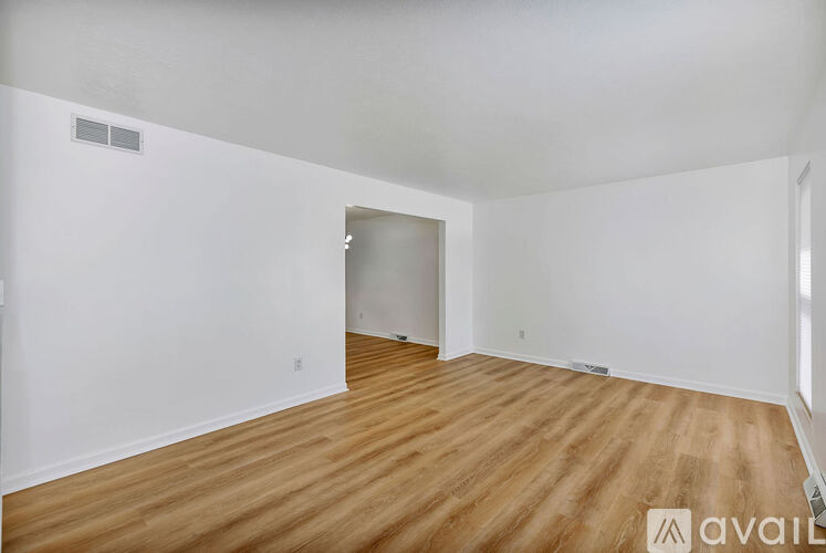 A room with wooden flooring and white walls, with a doorway leading to another room.