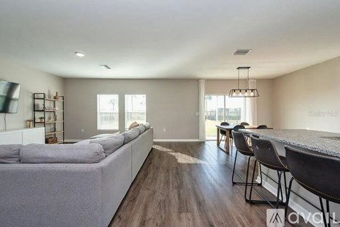 A spacious living room with a grey sofa and a dining table with chairs.