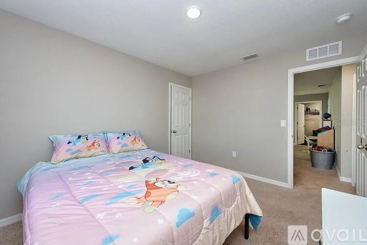 A bedroom with a bed covered in a pink blanket with cartoon characters on it.