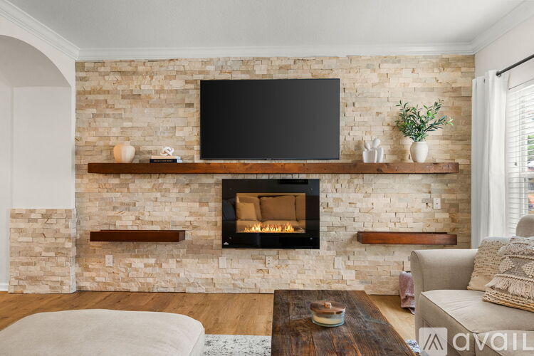 A living room with a stone fireplace and a flat screen TV mounted above it.