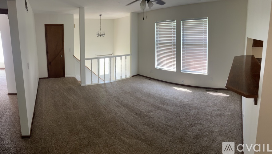 A spacious room with a carpeted floor, a ceiling fan, and a window with blinds.