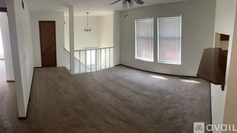 A spacious room with a carpeted floor, a ceiling fan, and a window with blinds.