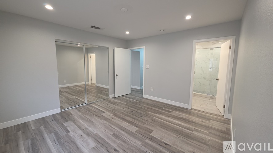 A room with wooden flooring and white walls, with a glass door leading to another room.