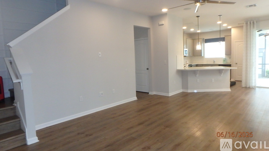 A spacious room with wooden floors and a staircase on the left side.