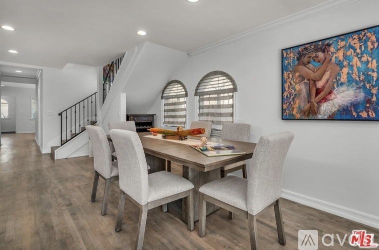 A dining room with a table and chairs and a painting on the wall.