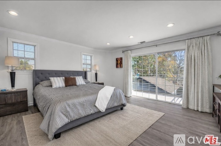 A bedroom with a large bed, a nightstand, and a sliding glass door leading to a balcony.