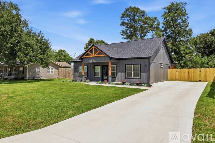 A modern house with a grey exterior and a brown roof is surrounded by a well-maintained lawn and a wooden fence.