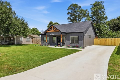 A modern house with a grey exterior and a brown roof is surrounded by a well-maintained lawn and a wooden fence.