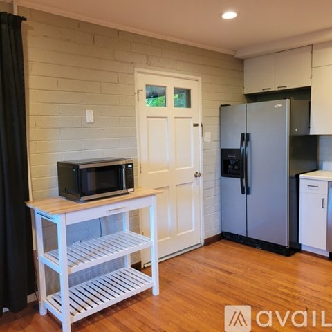 A kitchen with a white door, a microwave on a cart, and a refrigerator.