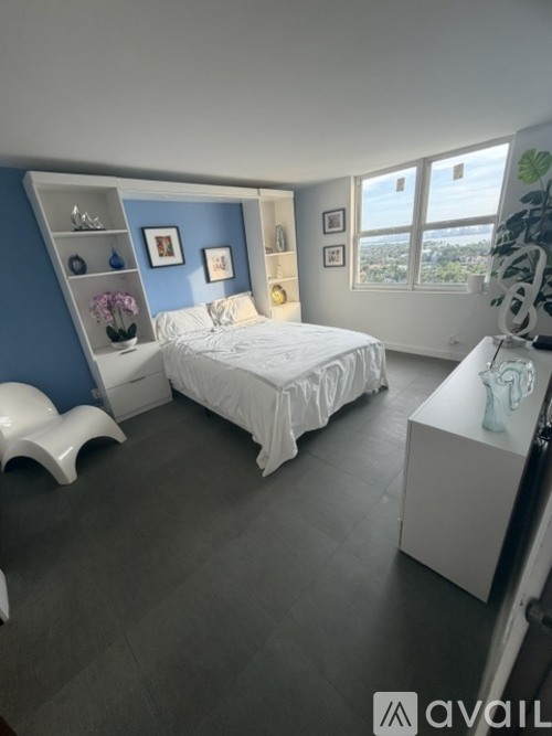 A bedroom with a bed, a nightstand, and a window overlooking a cityscape.