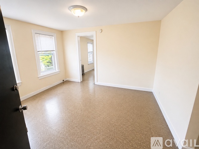 A room with a carpeted floor, a window with blinds, and a door leading to another room.