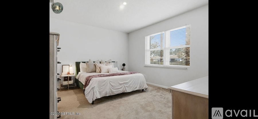 A bedroom with a large bed and a window with blinds.