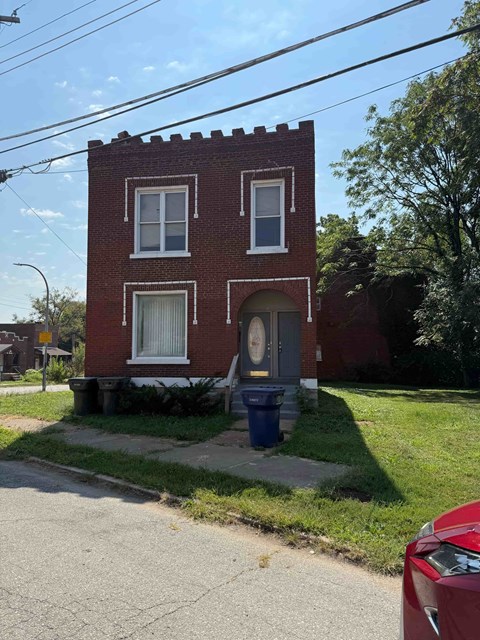 A red brick house with a blue trash can in front.