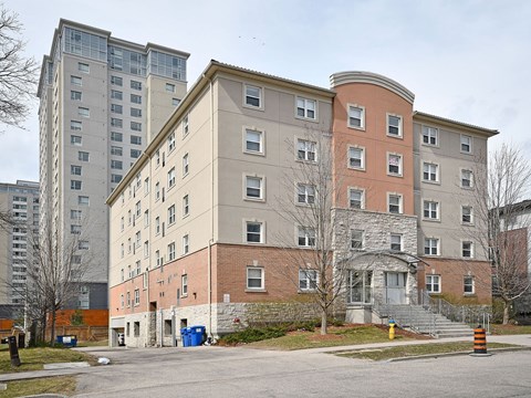 A large building with a red brick base and a grey top sits in front of a tall building.