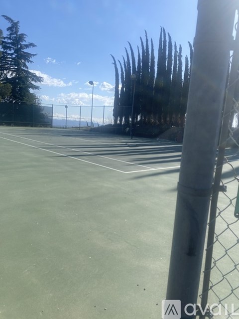 A tennis court with a fence and trees in the background.