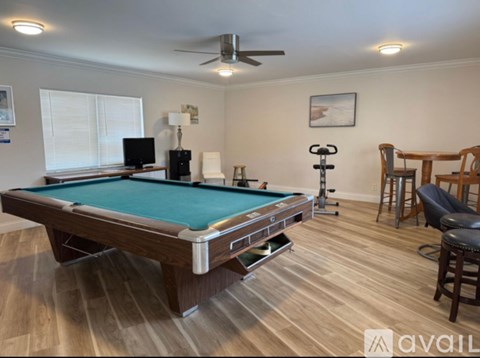 A pool table is in the middle of a room with wood flooring and a ceiling fan.