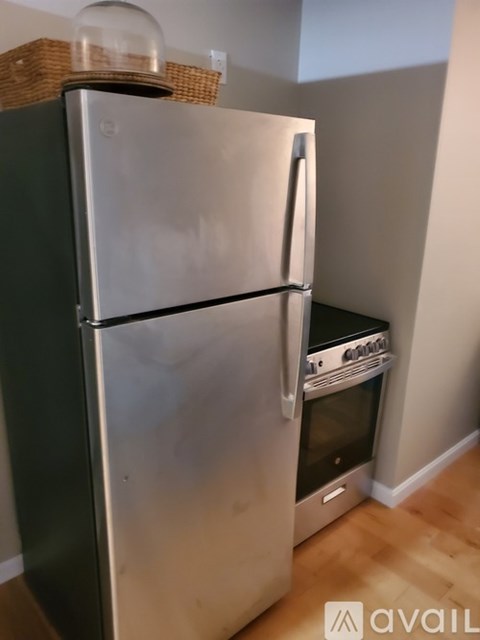 A stainless steel refrigerator with a black handle and a black door sits in a kitchen.