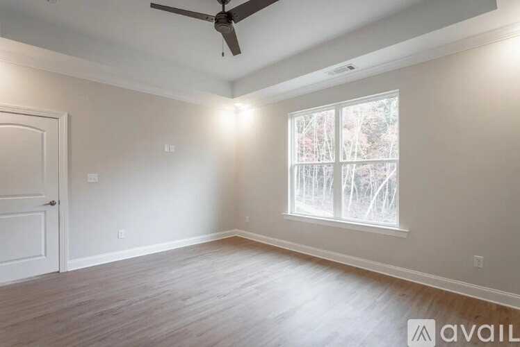 A room with a ceiling fan and a window showing trees outside.