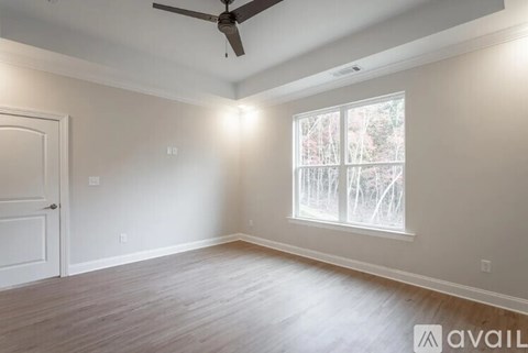 A room with a ceiling fan and a window showing trees outside.