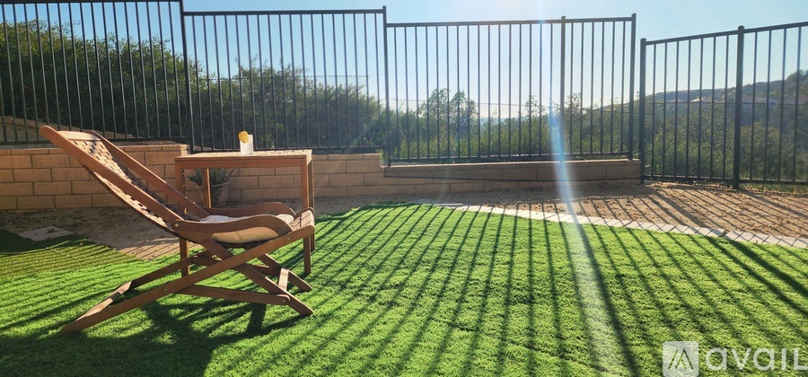 A wooden chair is on a lawn in front of a black fence.