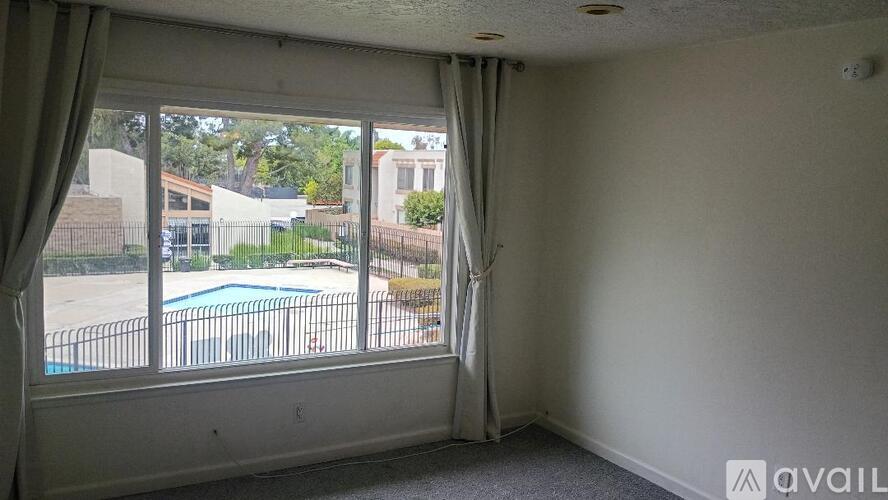 A room with a window overlooking a pool and a fence.