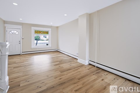 A room with wooden floors and white walls, with a door and a window.