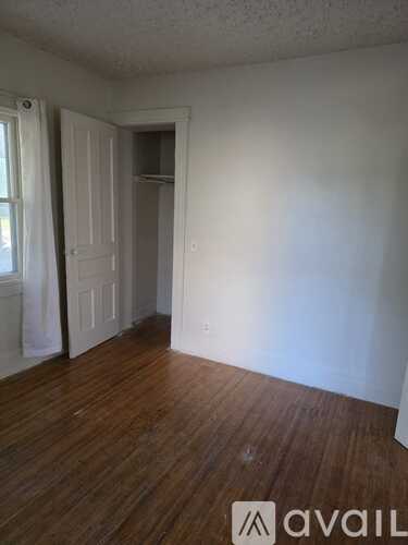 A room with wooden floors and white walls, with a door and a window.