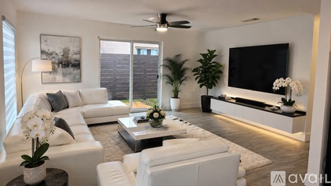 A living room with a white sofa set and a television mounted on the wall.