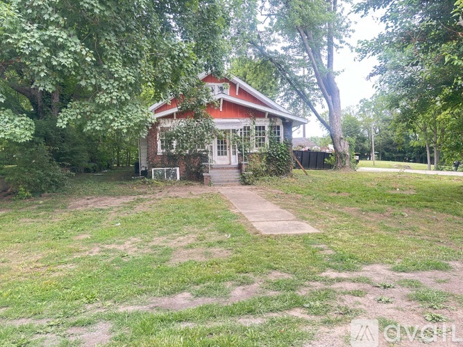 A red house with a white door and windows is surrounded by trees and grass.