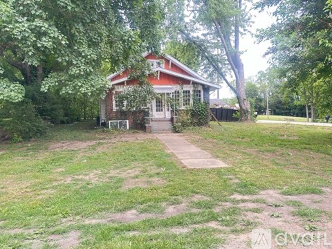 A red house with a white door and windows is surrounded by trees and grass.