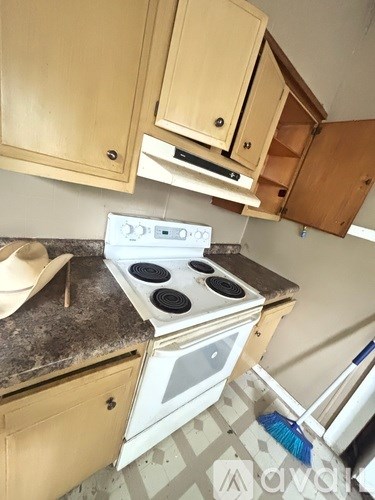 A white stove top oven with four burners is in a kitchen with wooden cabinets.