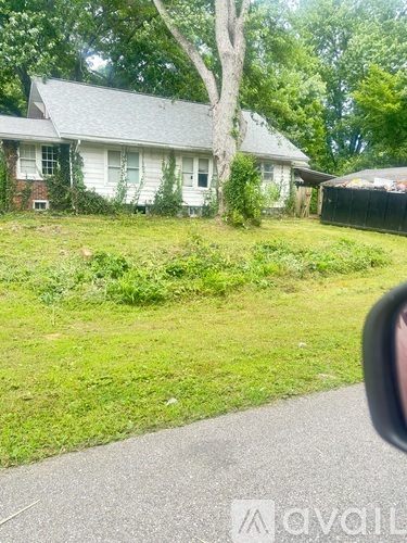 A white house with a grey roof and a tree in front of it.