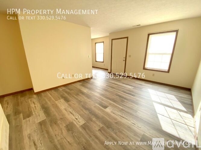 A room with wooden flooring and two windows, with a sign for HPM Property Management.