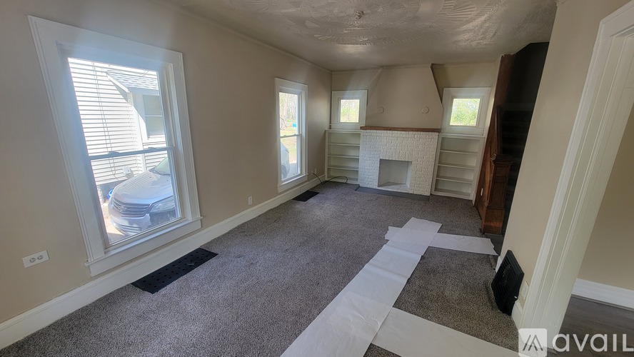 A room with a carpeted floor, a fireplace, and a window with blinds.