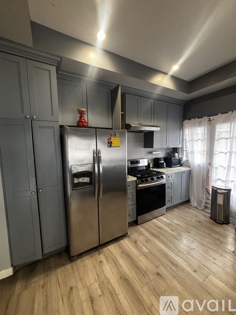 A kitchen with a stainless steel refrigerator, wooden floors, and grey cabinets.