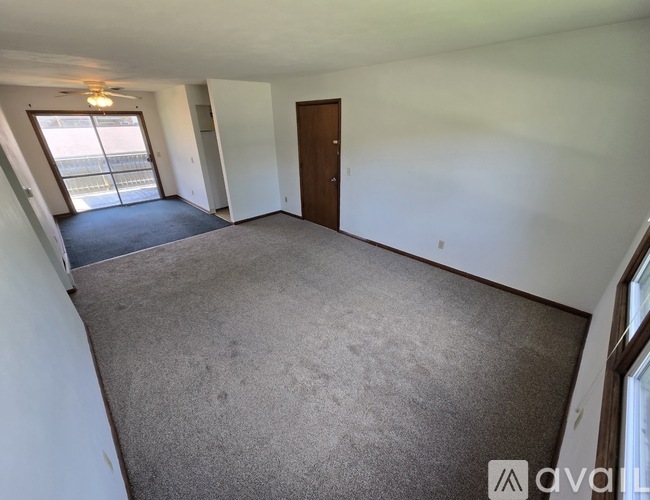 A spacious room with a carpeted floor, a ceiling fan, and a door leading to another room.