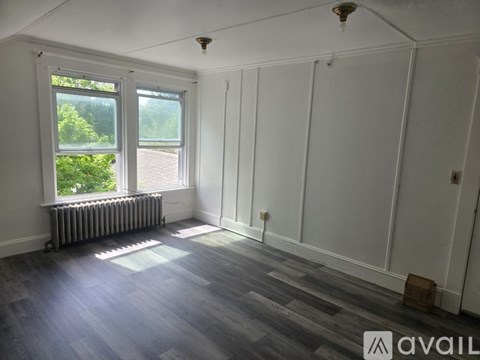 A room with white walls and a window with a view of trees and a fence.