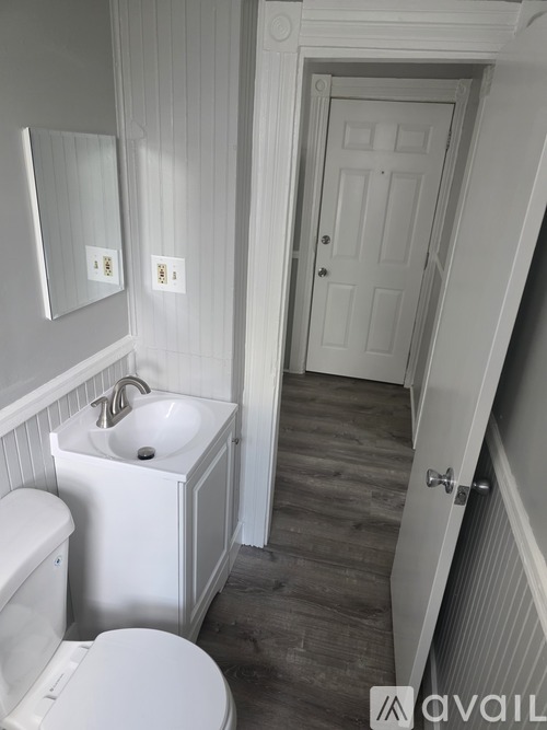 A bathroom with a toilet, sink, mirror and wooden floors.