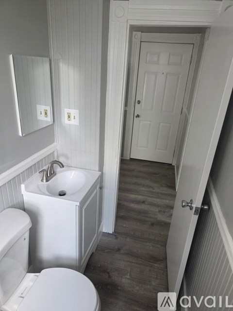 A bathroom with a toilet, sink, mirror and wooden floors.