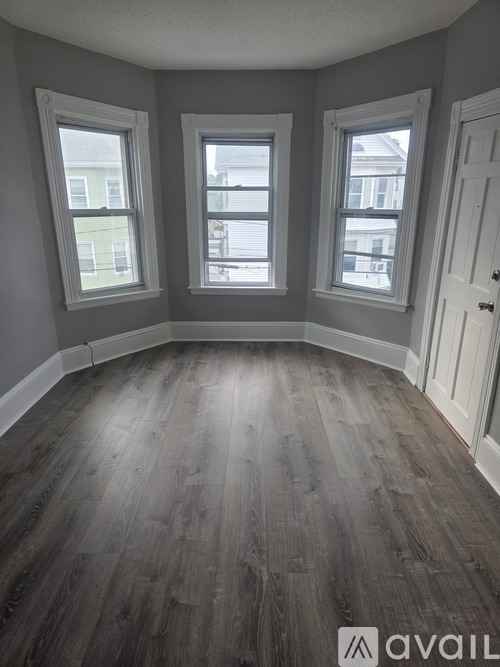 A room with grey walls and wooden flooring with three windows.
