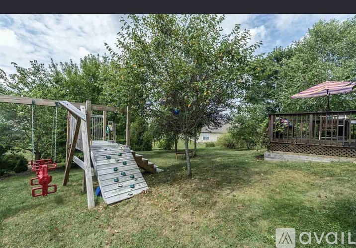 A wooden swing set with a red slide in a grassy backyard.