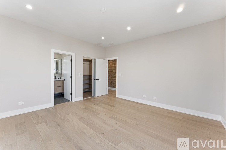 A spacious room with wooden flooring and white walls, with two open doors.