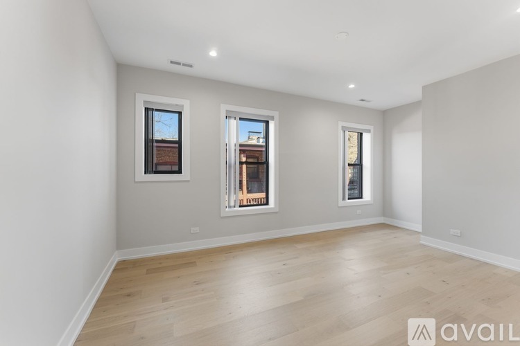 A spacious room with wooden flooring and three windows.