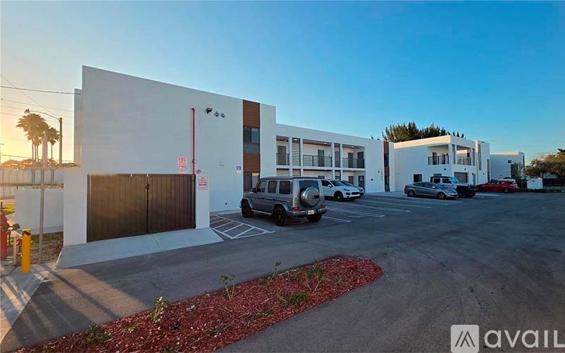 A parking lot with a white building and a red flower bed in front.