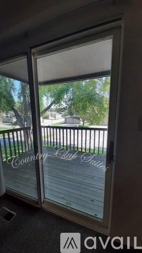 A sliding glass door with a view of a deck and trees outside.