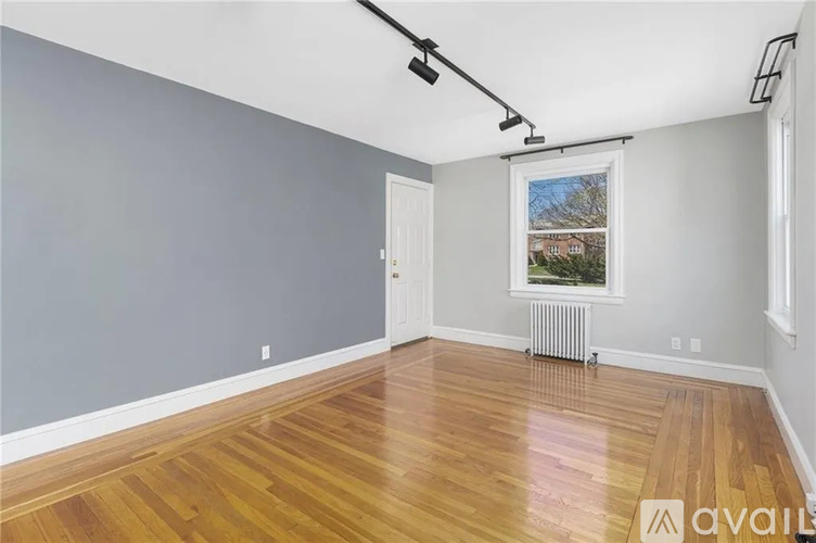 A room with wooden flooring and a window with a view of a house across the street.