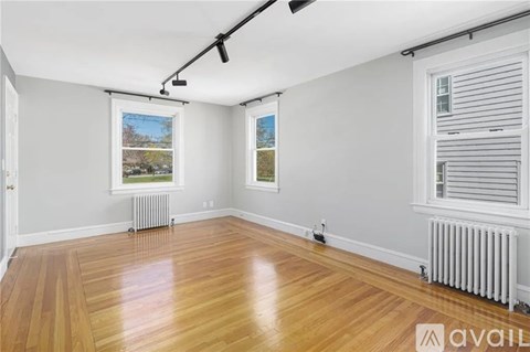 A room with wooden floors and white walls, with a window showing a view of trees and a radiator on the floor.