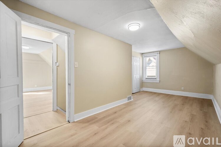 A room with wooden flooring and a window with a view of a building outside.