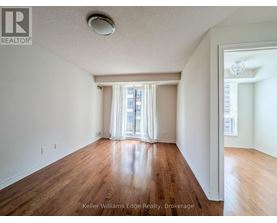 A spacious room with wooden floors and white walls, with a window covered by white curtains.