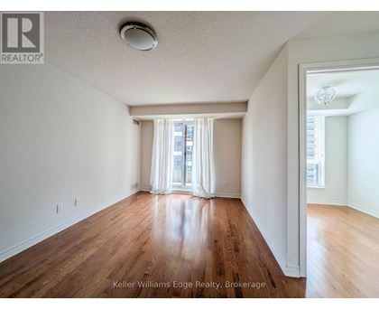 A spacious room with wooden floors and white walls, with a window covered by white curtains.